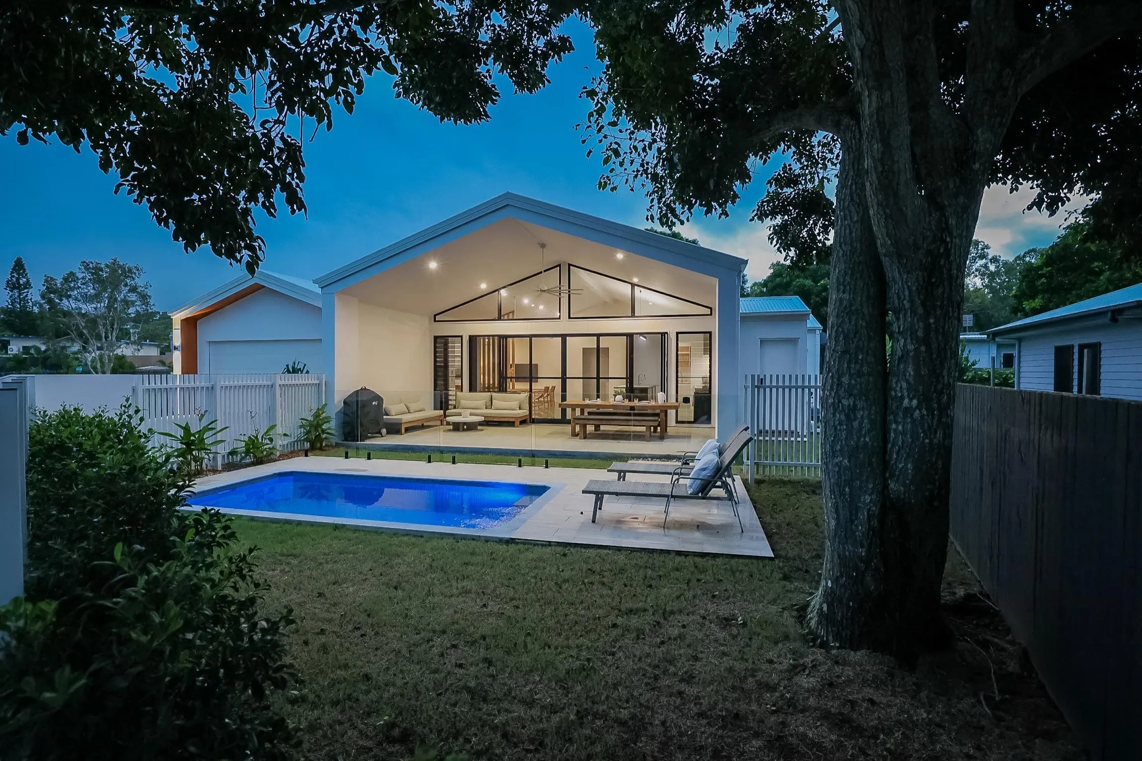 A tiled plunge pool glowing at dusk beside an open-plan outdoor living space